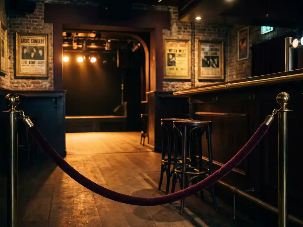 Fluwelen touw bij ingang van intiem Amsterdams muziekcafé met amber podiumlicht, houten bar en vintage concertposters op bakstenen muur.