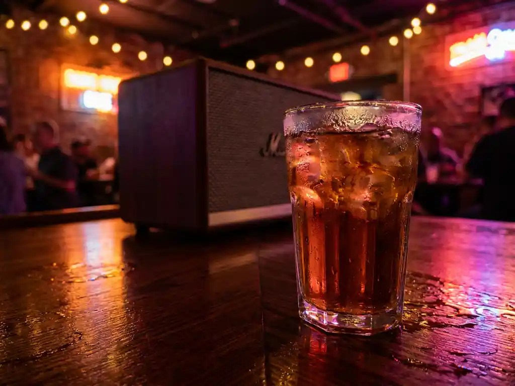 Beslagen glas met ijskoude cocktail op donker houten bar, omgeven door amberkleurig en magenta neonlicht in een Amsterdamse club.